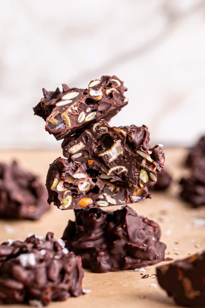 Pretzel Pumpkin Seed Date Chocolate Clusters stacked on top of one another, the the top 3 cut in half to reveal the pretzels, pumpkin seeds and dates inside the chocolate