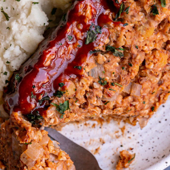 close up of Vegan Gluten-Free Meatloaf on a plate with mashed potatoes and a piece of meatloaf cut off with a fork