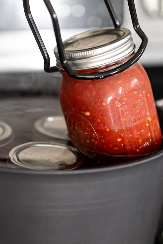 removing a jar of salsa from the boiling water with canning tongs