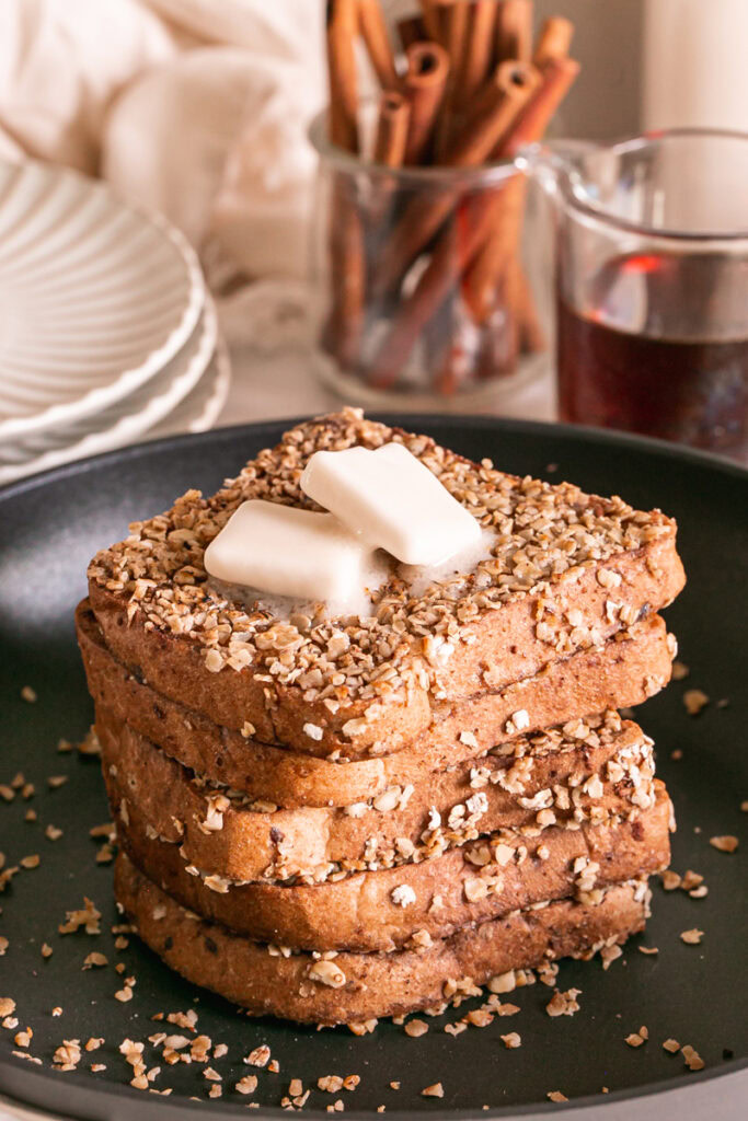 close up of pumpkin spice oat crusted French toast stacked in a skillet with two squares of butter on the top one