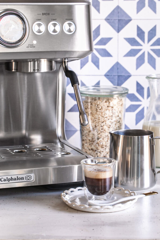 close up of the calphalon espresso machine with a glass of espresso in front and a jar of oats in the background