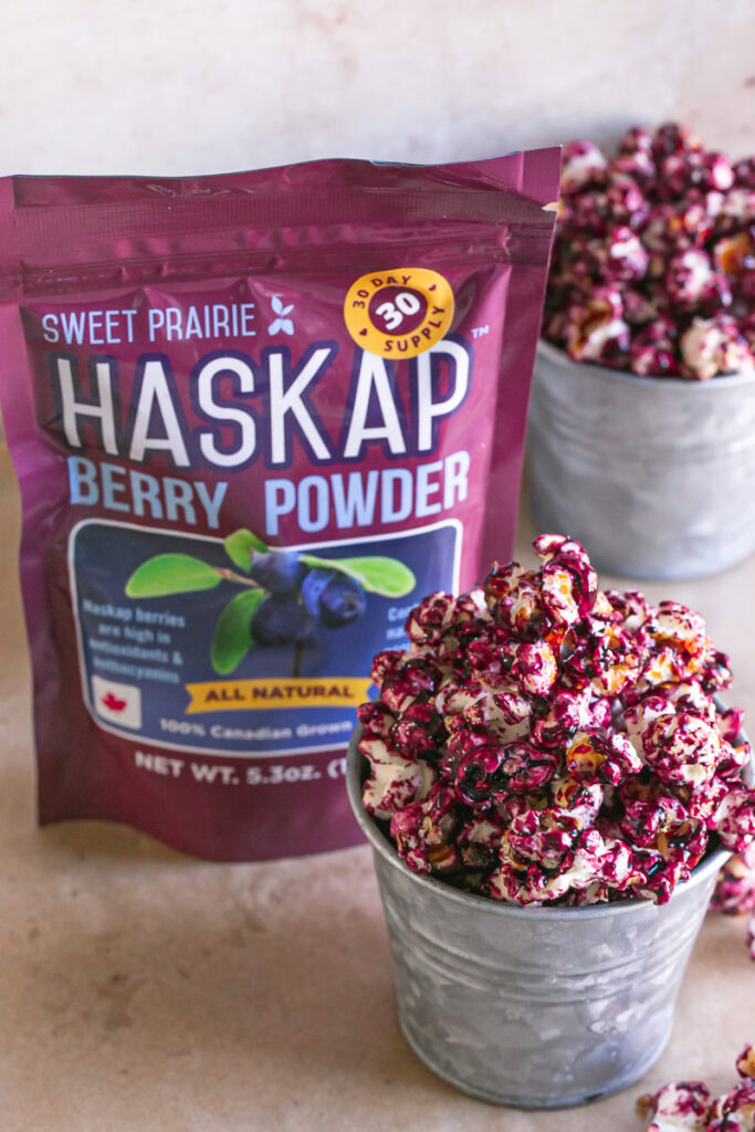 close up of Candied Haskap Berry Popcorn with a bag of sweet prairie haskap powder in the background