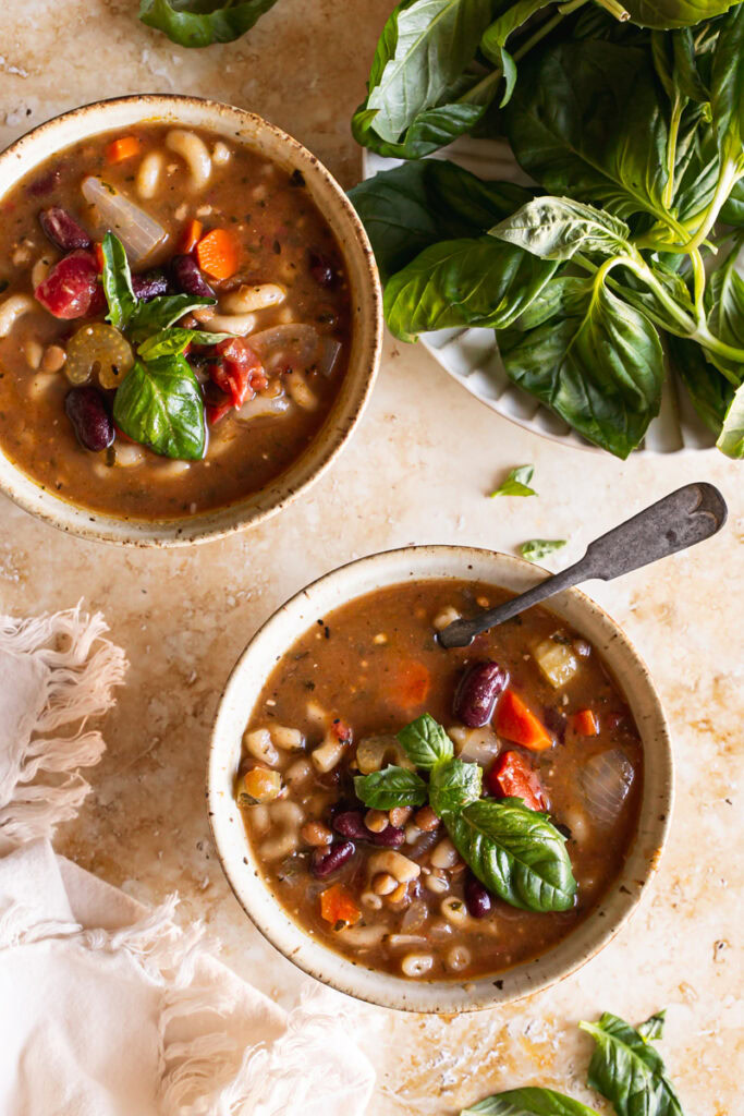 two bowls of plant based minestrone soup with a plate of fresh basil
