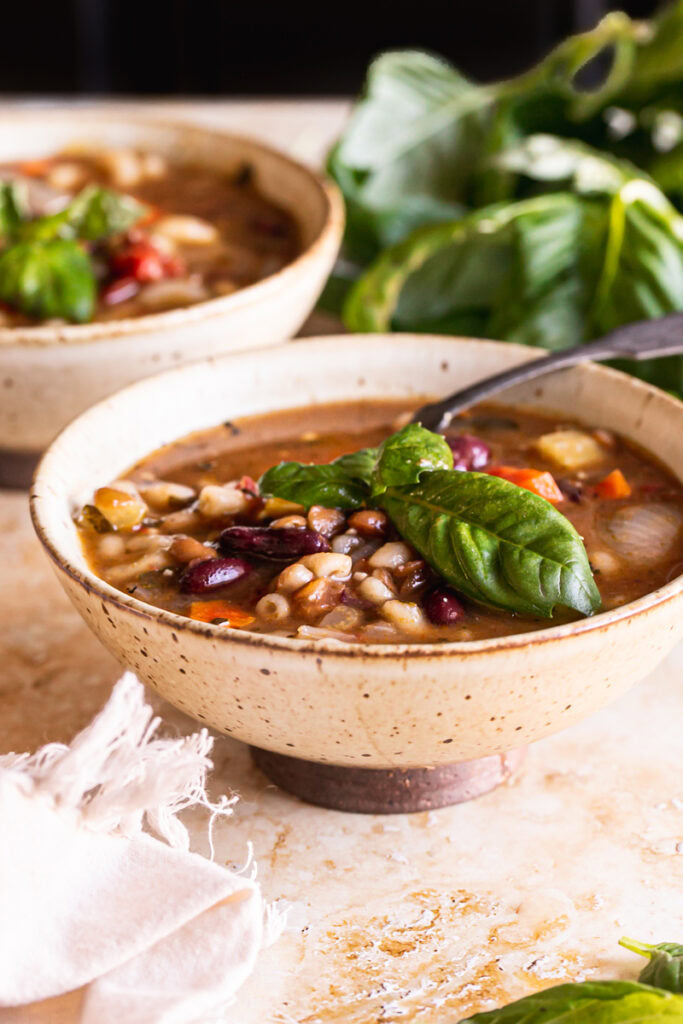 two bowls of plant based minestrone soup with a plate of fresh basil in the background