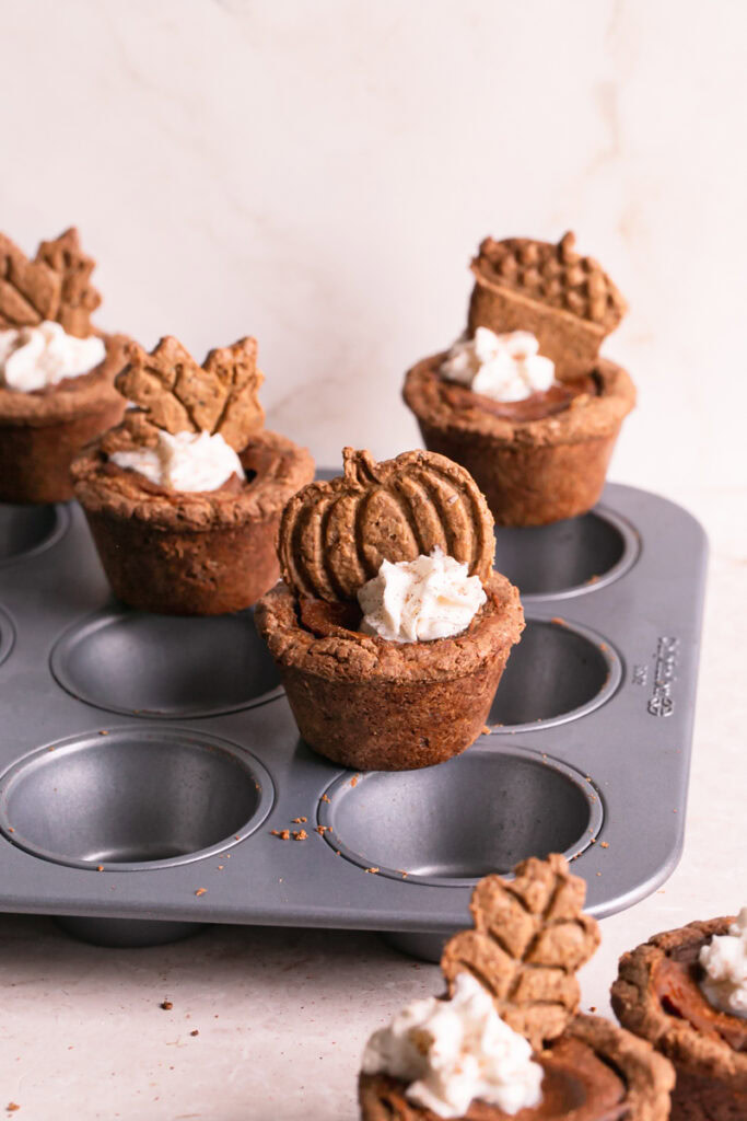 pumpkin pie cookie cups decorated with whipped cream and a cookie set on top of a calphalon muffin pan